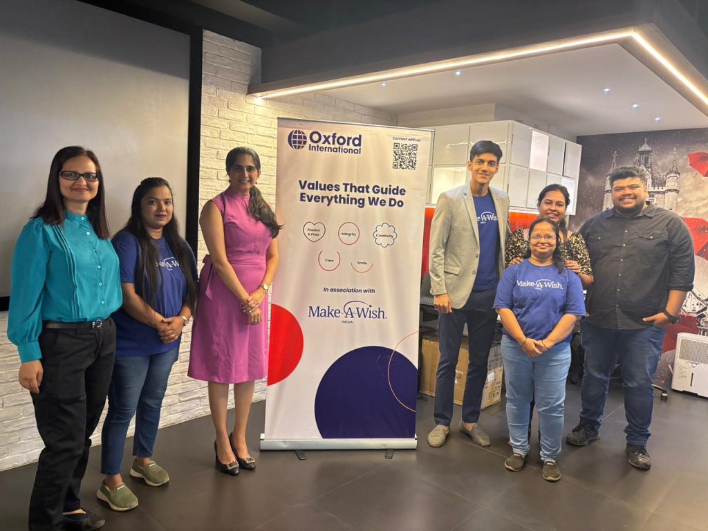 A group of colleagues from the Oxofrd International Indi office standing infront of a roll up banner that has the Oxford International logo and branding on it, alongside 'Values that Guide everything we do'